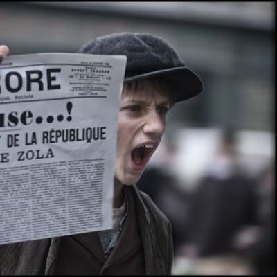 En pojke håller upp tidningen L'Aurore med löpsedelstexten: J'Accuse...!