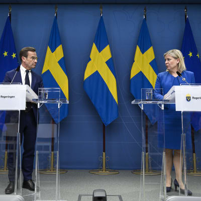 Moderatledaren Ulf Kristersson och Sveriges socialdemokratiska statsminister Magdalena Andersson framför varsitt podium med svenska och EU-flaggor i bakgrunden.