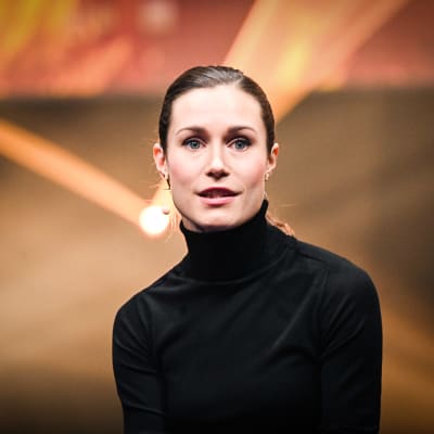 Statsminister Sanna Marin klädd i svart med en gul lampa i bakgrunden.