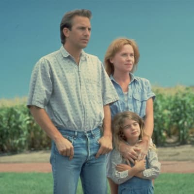 Mies, nainen ja pikkutyttö katsovat samaan suuntaan maissipellon edustalla.