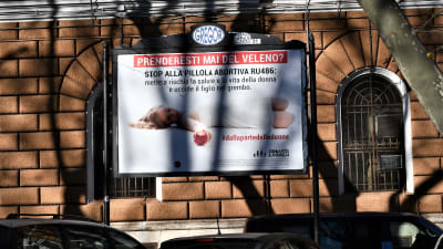 En affisch med italienska slagord mot abortpiller och en bild på en liggande kvinna på en husvägg.