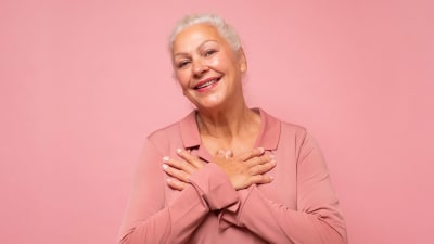 Leende äldre kvinna framför rosa bakgrund