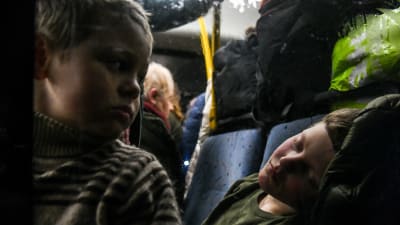 En pojke sover i en buss. En annan pojke sitter bredvid.