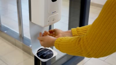 Två händer under en automat som doserar handsprit. 