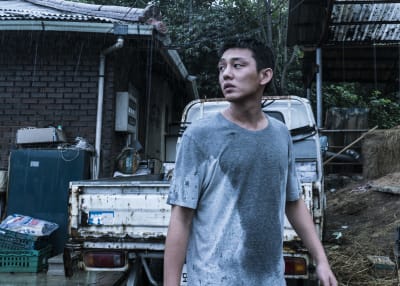 Nuori aasialainen mies hikinen paita päällä, taustalla autonrämä. Kuva elokuvasta Burning.