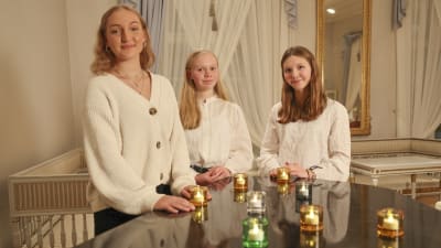 Tre unga kvinnor står vid en flygel och tittar in i kameran