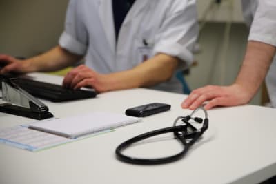Läkare sitter vid dator, på bordet även ett stetoskop.