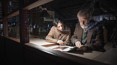 Otto (Amos Brotherus) och Olavi (Heikki Nousiainen) sitter i arkivet och tittar på gamla utställningskataloger.