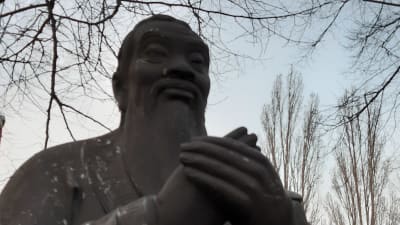 Övre delen av Konfuciusstaty, står med händerna ihop, blickar ut