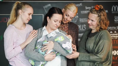 På bilden ses fyra kvinnor där en av kvinnorna håller i en bebis i en filt. 