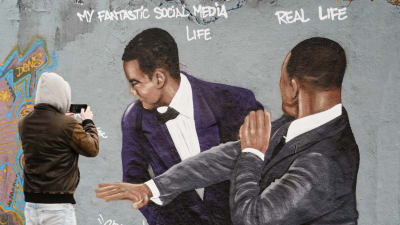 En väggmålning där Will Smith slår Chris Rock. En man tar en bild av målningen.