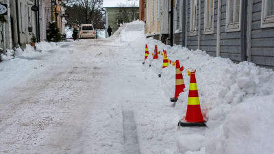 Trafikkoner står invid en husvägg på en snöig gata i Gamla stan i Borgå.
