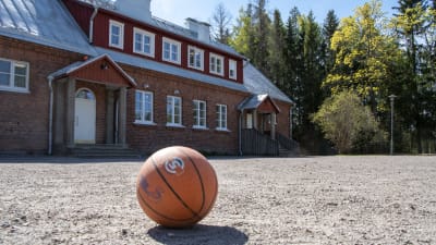 En baskeboll ligger på sandplanen framför Södra Paipis skola och förskola.