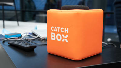 En orange, mjuk kub står på ett bord. Utanpå den står det catch box.