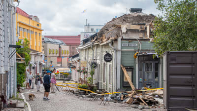 Personer på gata tittar på en träbyggnad som förstörts i en brand. 