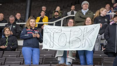 Två personer håller upp ett lakan som det står ToBK på.