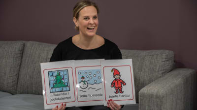 Sandra är glad och håller i tre olika bilder. En bild på en tomte, att det snöar och en julkalender.