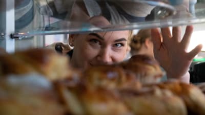närbild på Irenes ansikte som tittar igenom luckan där de serveras bullor och bakverk.