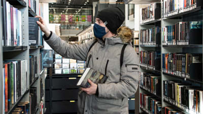 Wilhelm är på biblioteket och plockar en bok ur hyllan.