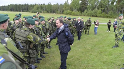 Statsminister Stefan Löfven, med försvarsminister Peter Hultqvist i bakgrunden hälsade på soldater under militärövningen Aurora  i september 2017.
