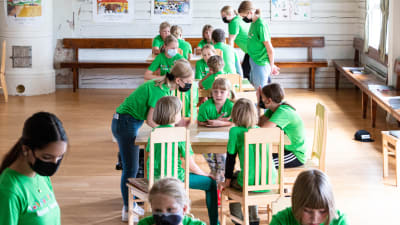 Barn som sitter vid bord i en sal.