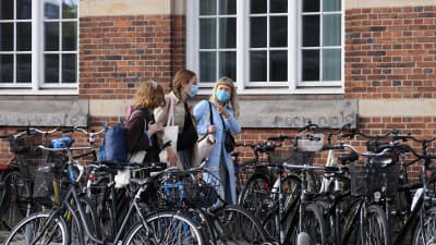 Ungdomar går på en gata med många parkerade cyklar. De bär munskydd.