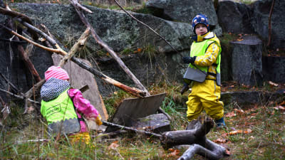 En flicka och en pojke från dagisgruppen Valhajarna bygger en koja av kvistar och träbitar vid en klippa på Drumsö.