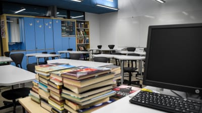 Böcker och laptop i förgrunden, tomt klassrum i bakgrunden
