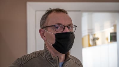En man med svart munskydd tittar in i kameran