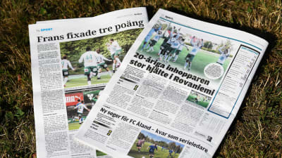 Ålandstidningen och Nya Åland ligger på en gräsmatta. I tidningarna står det om Frans Grönlunds segermål för IFK Mariehamnn borta mot RoPS. "Frans fixade tre poäng" och "20-åriga inhopparen stor hjälte i Rovaniemi".