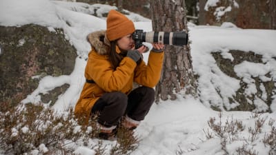 Anette sitter på huk i snön och tar en bild med sin systemkamera.