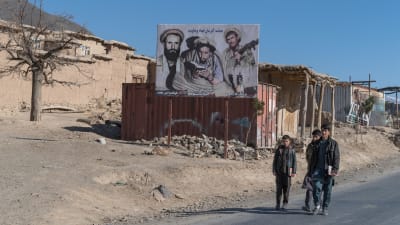 Unga män går förbi befälhavare Massouds porträtt i Panjshirdalen, Afghanistan