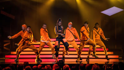 Kvinna omgiven av manliga dansare i orange