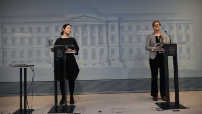 Emma Kari och Krista Mikkonen står vid var sitt podium på en presskonferens.