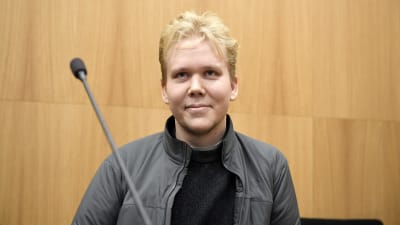 Aleksanteri Kivimäki är en blond ung man med kort hår. Han sitter i rätten och ler.