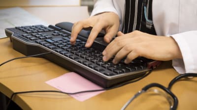En person i läkarrock skriver på ett tangentbord.