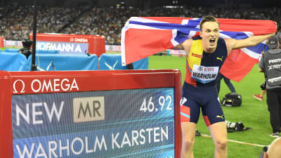 Karsten Warholm jublar med norska flaggan framför en resultatskärm som berättar om hans supertid.