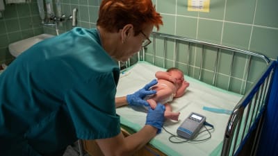 Barnmorskan Mervi Lanu mäter nyfödda Ronjas puls. Ronja ligger med blöja på skötbordet. 