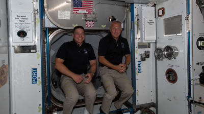 Bild på två män som sitter i en rymdraket. De ler mot kameran.