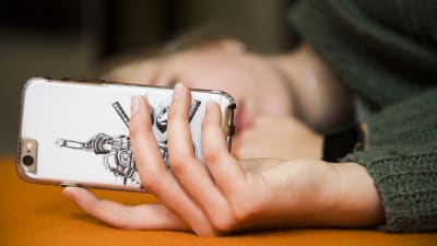 Flicka ligger på en soffa och ser på mobiltelefonens skärm.