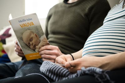 Raskaan olevan henkilö lukee kumppaninsa kanssa "Meille tulee vauva" kirjaa.