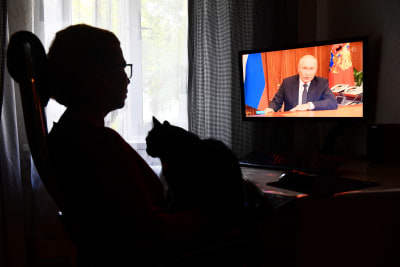 En person som ser på en tv, där ett tal med Vladimir Putin sänds.