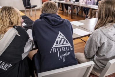 Tre ungdomar, den mittersta har en collegeskjorta på sig med Borgå svenska församlings ungdom-logo.