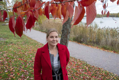 Jenny Högström har en röd jacka och står under ett träd med röda löv vid Hammars strand.