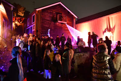 En mängd ungdomar deltar i ett Halloweenevenemang som ordnas bland gamla trähus.