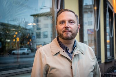 En man i beige jacka tittar in i kameran