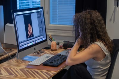 Anette sitter vid sitt skrivbord och editerar bilder på nakna kvinnokroppar.