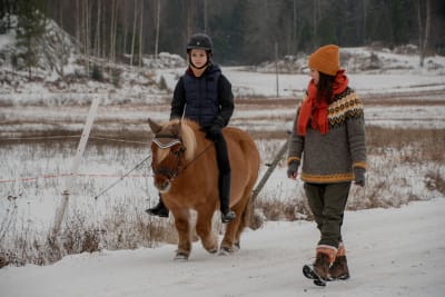 Anettes dotter rider på en ponny, Anette går bredvid. De rider på en väg vid åkerkanten, det är snö på marken.