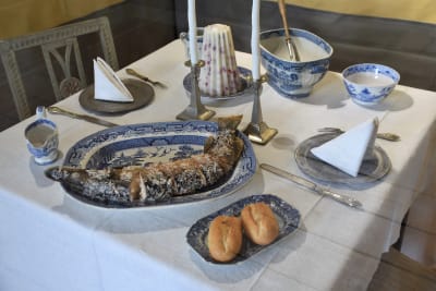 Bord i 1700-talsstil dukat i blå-vitt porslin med en ugnsstekt gädda och två semlor.