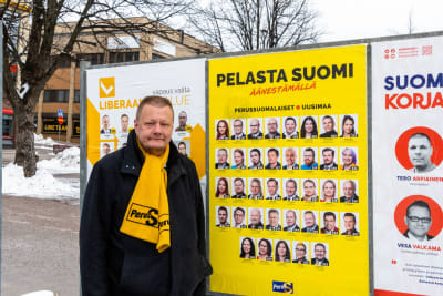 Sannfinländarnas Kevin Servin står framför partiets valplakat på Borgå torg.